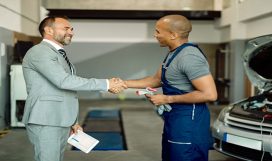 Happy black auto mechanic handshaking with a businessman while greeting in a workshop. Focus is on businessman.